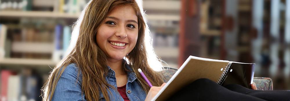 关于皇冠博彩 Student in the library writing notes on notebook