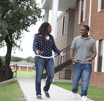 Two students walking on the sidewalk next to the dorm